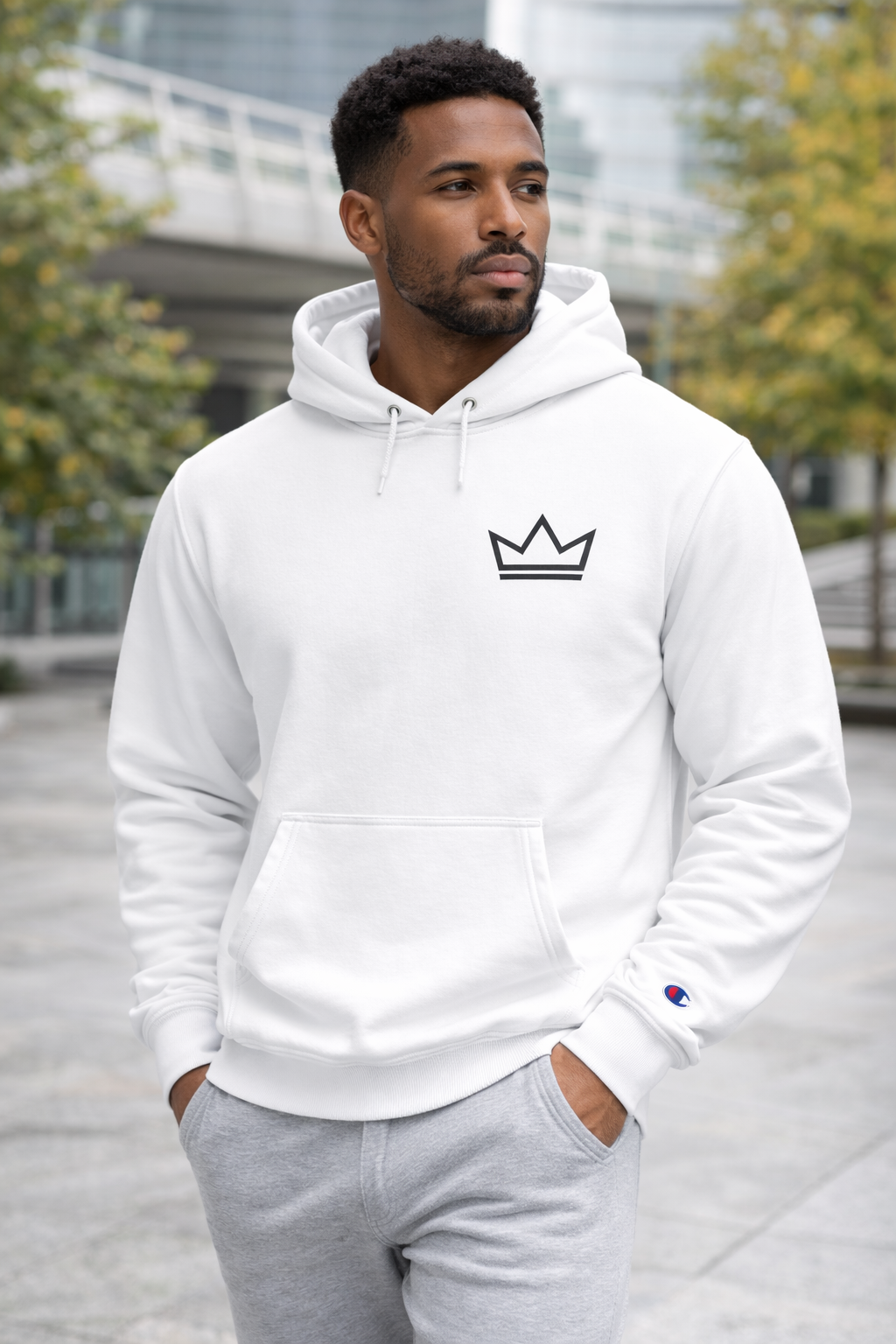 Male model wearing the white Ascension Hoodie by PurposeDriven, featuring a minimalist crown logo in an outdoor urban setting.