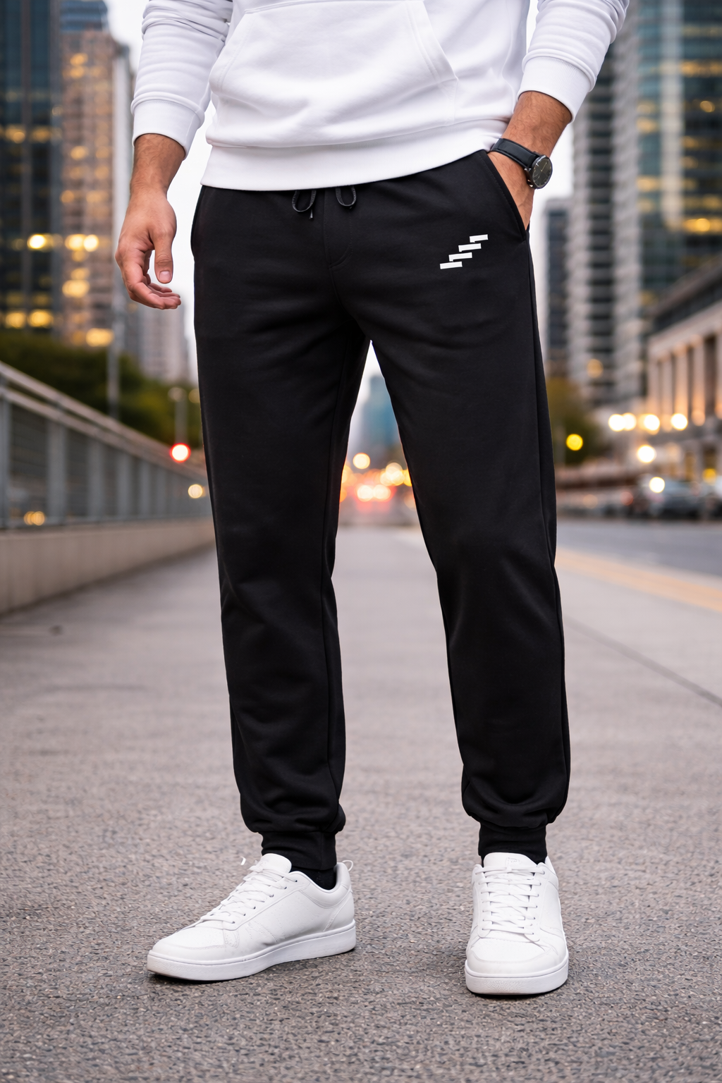 Men’s black Echelon premium fleece sweatpants worn with white sneakers, featuring ribbed cuffs and minimalist logo in an urban street setting