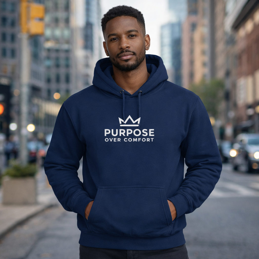 Man wearing navy blue Purpose Over Comfort hoodie with crown logo, minimalist motivational streetwear in urban city setting