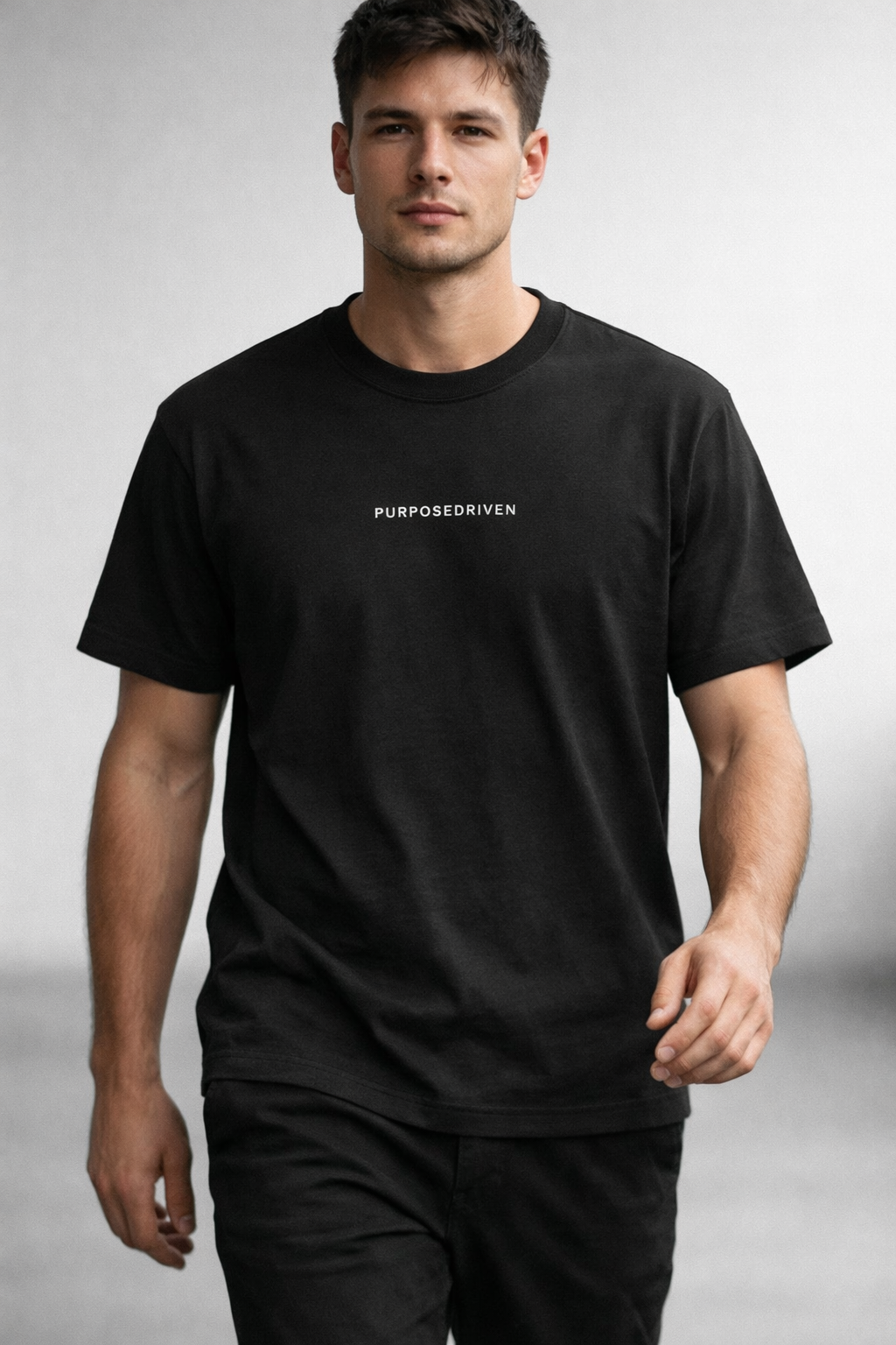 Male model wearing black PurposeDriven minimalist t-shirt, premium motivational streetwear on light neutral background