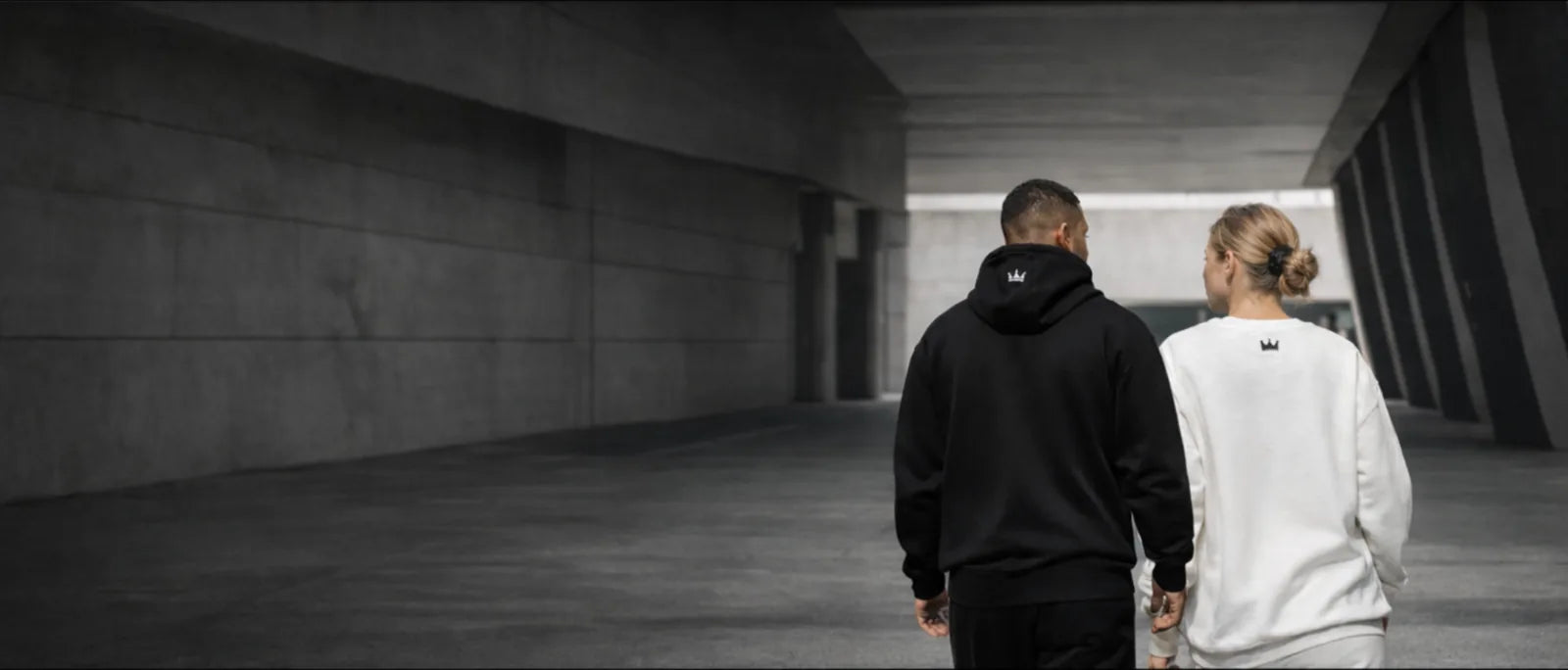 Man and woman walking through modern concrete corridor wearing minimalist black and white PurposeDriven hoodies, representing intentional streetwear designed for focus, discipline, and everyday purpose